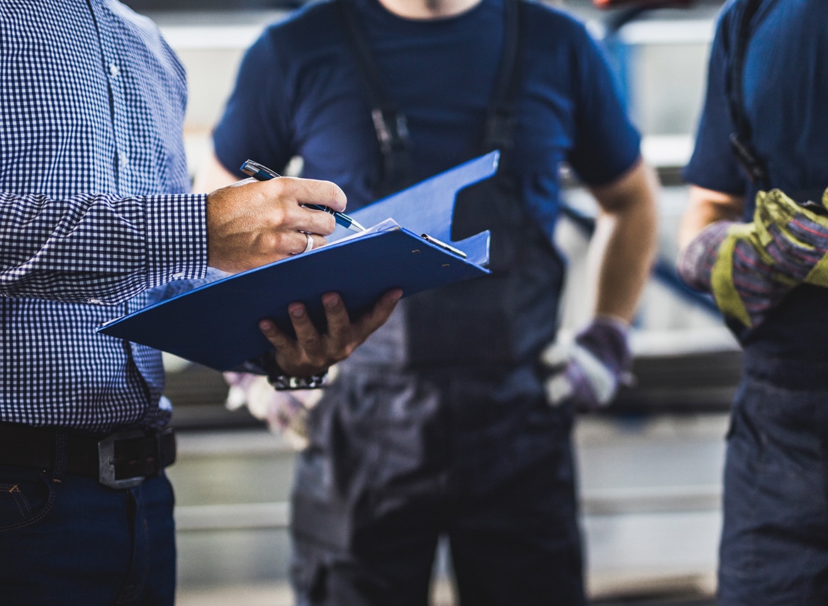 Unrecognizable foreman going through paperwork with manual workers in a warehouse.