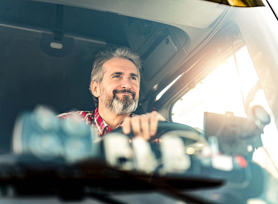 Happy mature truck driver driving his truck on a sunny day.